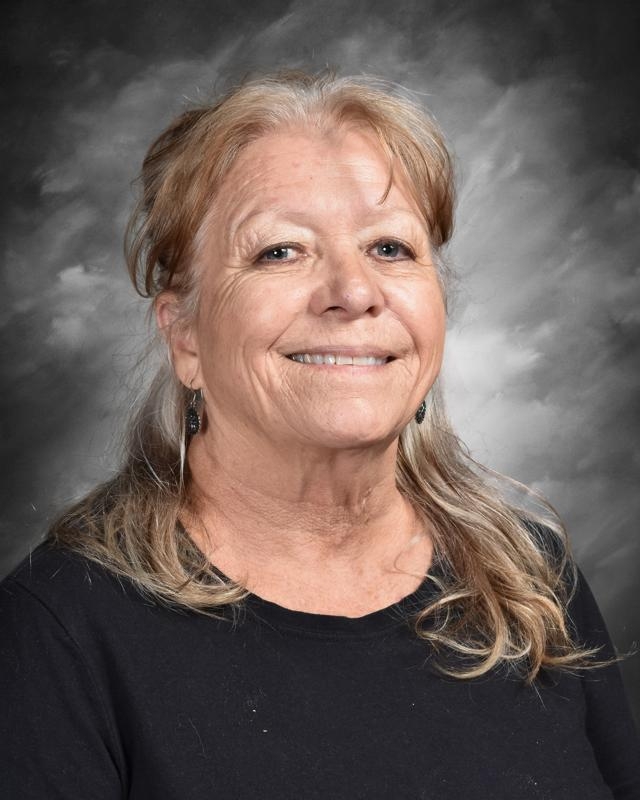 Smiling woman with long hair in a black shirt, set against a cloudy background.