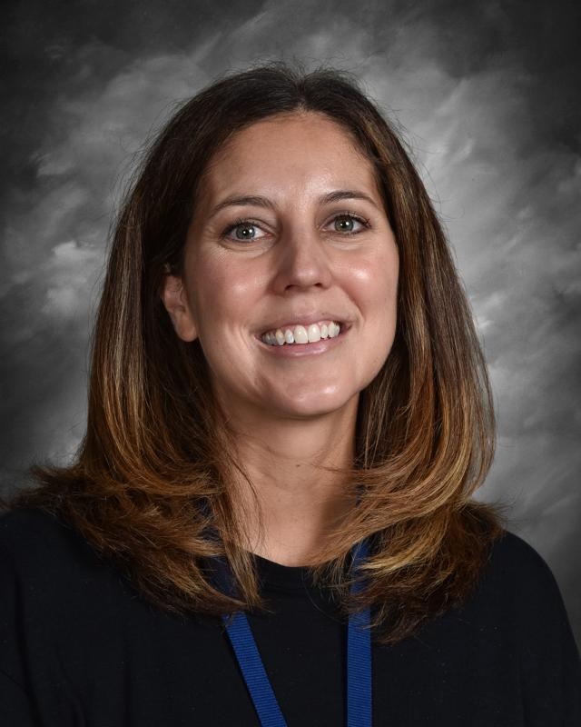 Smiling woman with shoulder-length hair wearing a black top and blue lanyard, gray background.