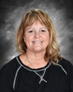 Smiling woman with shoulder-length hair wearing a black top and necklace, against a gray background.