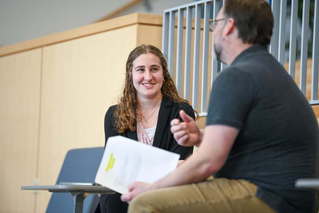 A woman with curly hair smiles while engaged in conversation with a man in a casual setting.