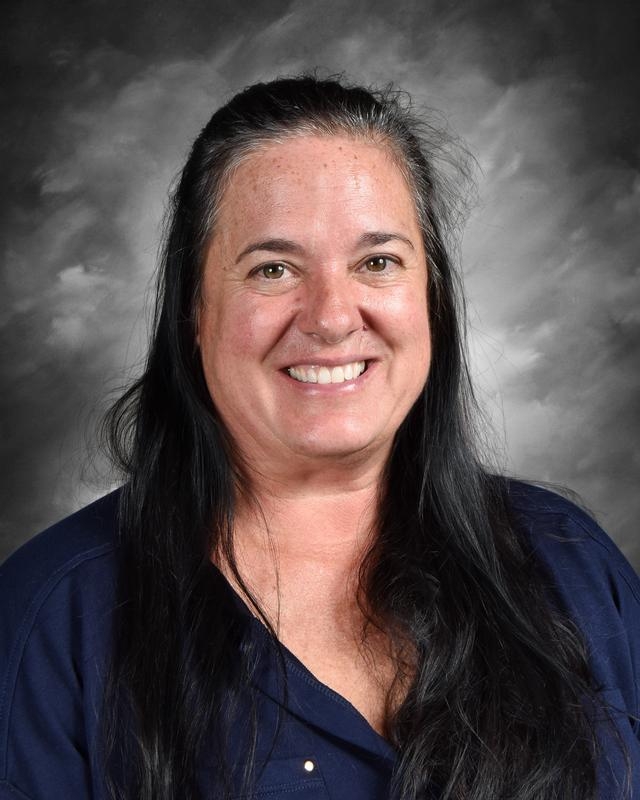 Smiling woman with long black hair, wearing a dark shirt, against a gray background.