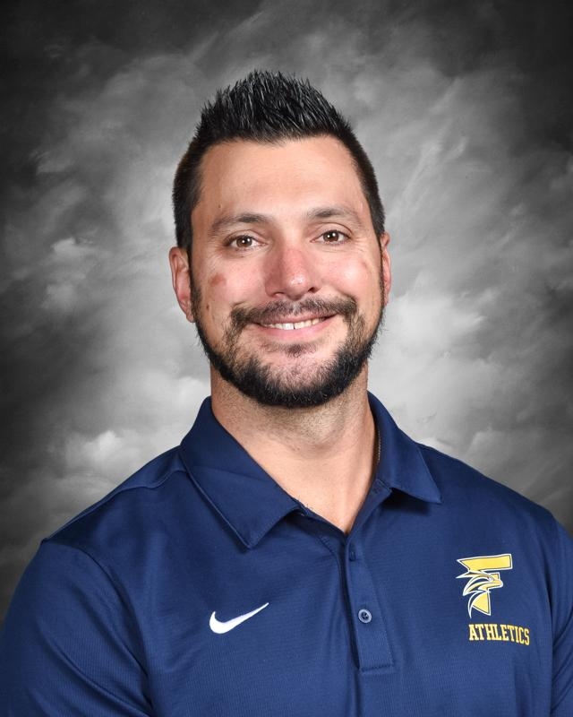 Smiling man with short dark hair and beard, wearing a blue "Athletics" polo shirt.